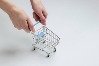 Minimalizm alışveriş konsepti. Kadın elleri beyaz arka planda mini alışveriş arabası tutuyor.