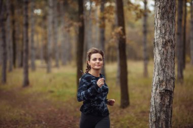 Sonbahar ormanında koşu. Spor giyimli genç bir kadın orman yolunda koşuyor. Sağlıklı yaşam tarzı kavramı