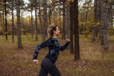 Sonbahar ormanında koşu. Spor giyimli genç bir kadın orman yolunda koşuyor. Sağlıklı yaşam tarzı kavramı