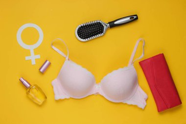 Sarı arka planda sütyen ve kadın aksesuarları. Kadın giysisinin yukarıdan görünüşü. Moda kadın kıyafetleri. Düz yatış, üst görünüm.