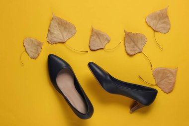 Beyaz arka planda yüksek topuklu deri ayakkabılar ve sarı arka planda kurumuş sonbahar yaprakları. Sonbahar koleksiyonu. Üst görünüm