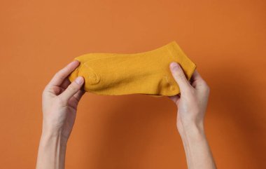 Kadın eli, kahverengi arka planda turuncu çorap tutar. Üst görünüm