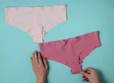 Kadın elleri, mavi bir stüdyo arka planında saten külotları katlıyor. Üst görünüm