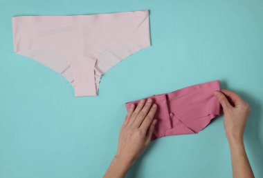 Kadın elleri, mavi bir stüdyo arka planında saten külotları katlıyor. Üst görünüm