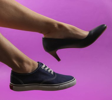 Mor arka planda topuklu ve spor ayakkabılı ince kadın bacakları. Yaratıcı moda çekimi