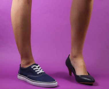 Mor arka planda topuklu ve spor ayakkabılı ince kadın bacakları. Yaratıcı moda çekimi