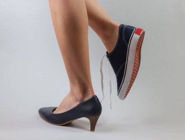 Zayıf kadın bacakları, topuklu ayakkabılar ve beyaz arka planda spor ayakkabılar. Yaratıcı moda çekimi