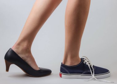 Zayıf kadın bacakları, topuklu ayakkabılar ve beyaz arka planda spor ayakkabılar. Yaratıcı moda çekimi