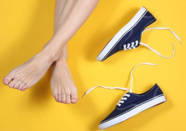 Sarı arka planda spor ayakkabılı kadınların çıplak ayakları. Üst görünüm