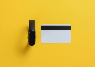 Sarı arka planda akıllı bilezik ve banka kartı. Temassız ödeme. Üst Manzara. Minimalizm