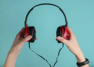 Kadın eli, mavi pastel arka planda şık telli kulaklıklar tutar. Müzik hayranı, DJ. Üst görünüm.