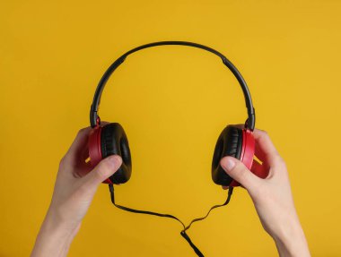 Kadın eli sarı pastel arka planda şık telli kulaklıklar tutar. Müzik hayranı, DJ. Üst görünüm.
