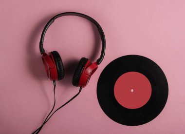 Pembe pastel arka planda vinil plaklı telli kulaklıklar. Retro tarzı DJ. Üst görünüm, minimalist müzik konsepti.
