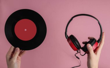 Kadın eli, pembe pastel arka planda vinil plaklı telli kulaklıklar tutuyor. Retro tarzı DJ. Üst görünüm, minimalist müzik konsepti.