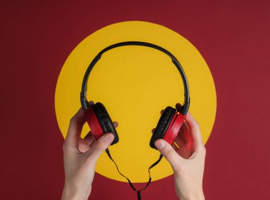 Kadın elleri kırmızı arka planda sarı daireli şık kulaklıkları tutuyor. Müzik hayranı, DJ. Üst görünüm.