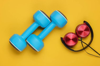 Minimalist spor ve fitness konsepti. Sarı arka planda telli kulaklık ve dambıl.