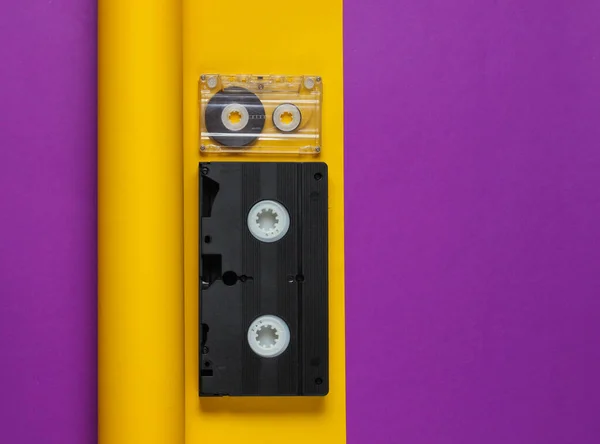 Video and audio cassette on yellow purple paper background. Color trend, minimalistic retro 80s still life. Top view