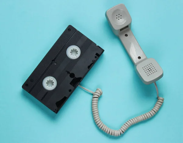 Phone handset and video cassette on blue paper background. Minimalistic retro still life. Top view