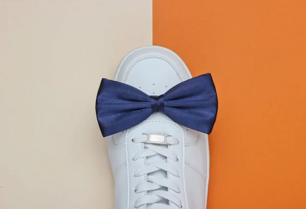 Stylish white sneaker with a bow-tie on a two-color paper background. Minimalistic fashion concept. Top view