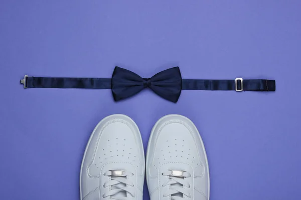 Stylish white sneaker and bow-tie on purple paper background. Minimalistic fashion concept. Top view