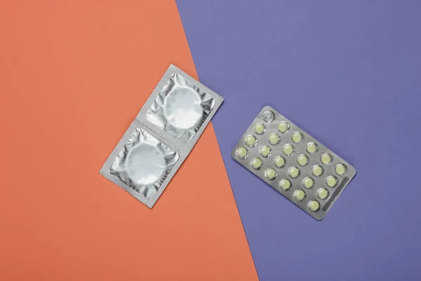 Condoms in packaging, birth control pills on a colored background. Top view. The concept of sexual preservation