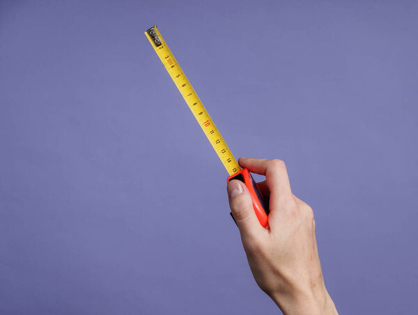 Female hands take measurements with industrial tape measure on purple background