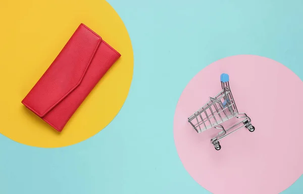ミニマリズムのショッピングコンセプト ショッピングトロリー 赤い革財布上のカラーペーパー背景 — ストック写真