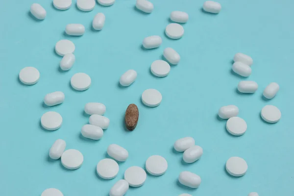 Lot of white pills and one herbal pill on a blue background.