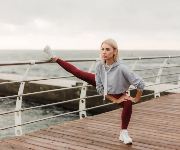 健康的生活方式概念 身穿运动服的年轻貌美女子在日出时在海滩上锻炼前做伸展腿运动 — 图库照片