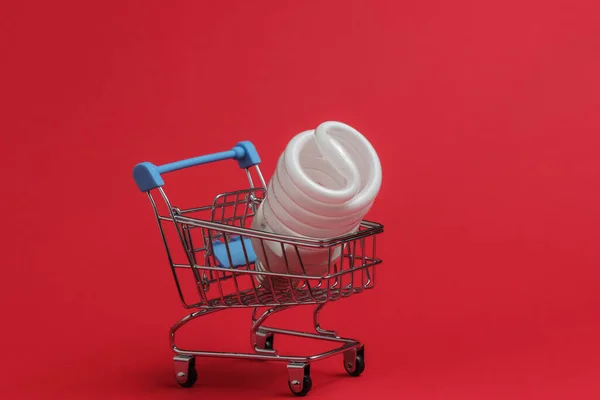 ショッピング エココンセプト 赤い背景に螺旋状の電球でショッピングトロリー — ストック写真