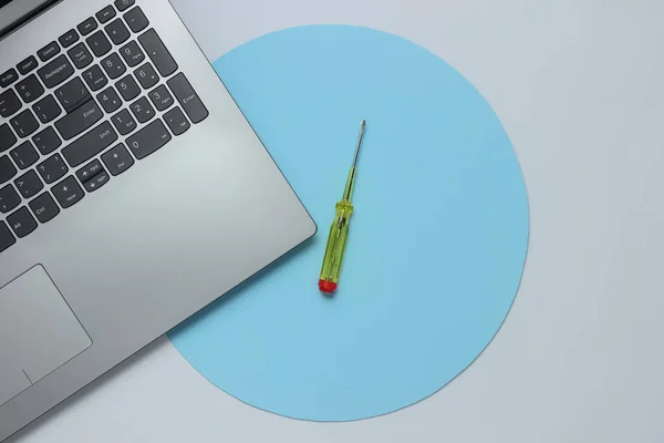 Service center, laptop repair. Laptop, screwdriver on white background with blue circle. Top view