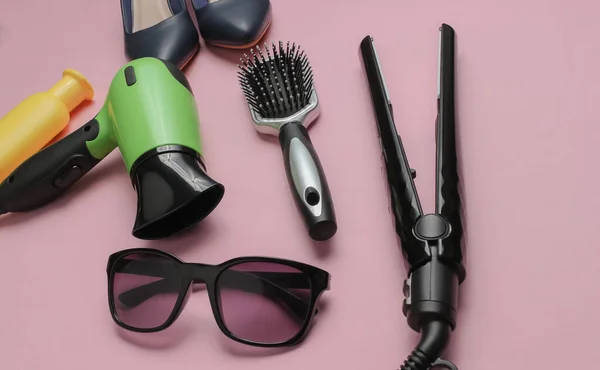 Women's accessories. Hair care. Beauty studio shot. Hair dryer, straighteners, bottle shampoo, comb, sunglasses, high heel shoes on pink pastel background.