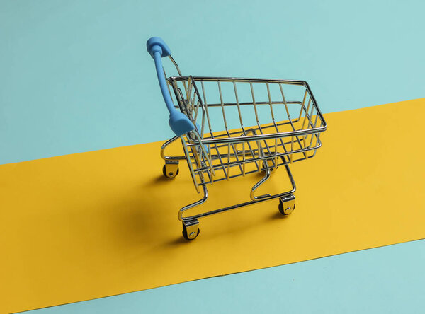 Minimalistic shopping concept. Shopping trolley on a blue-yellow background.
