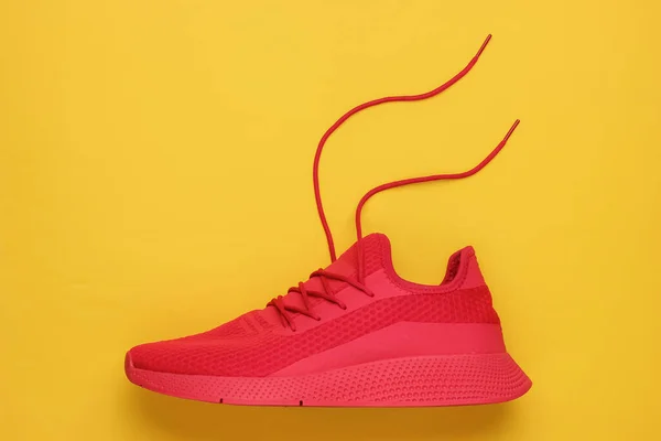 Red sport running shoe with untied laces on yellow background. Top view
