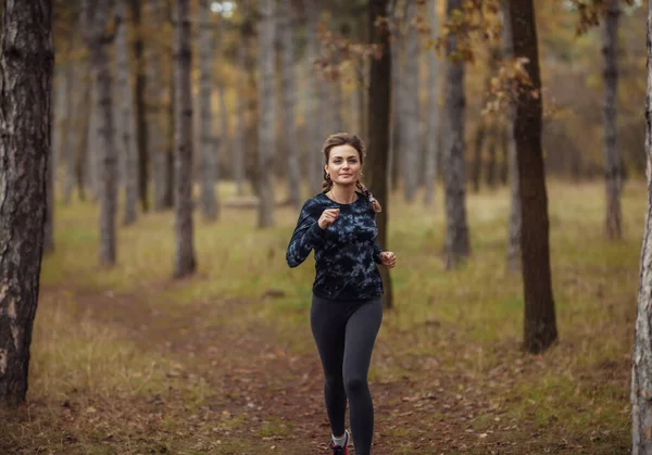 Sonbahar ormanında koşu. Spor giyimli genç bir kadın orman yolunda koşuyor. Sağlıklı yaşam tarzı kavramı