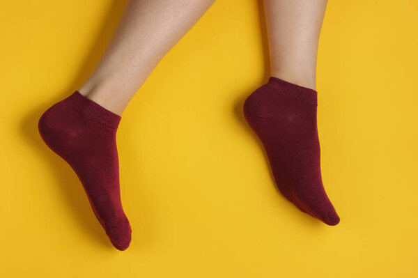 Женские тонкие ноги в бордовых носках на жёлтом фоне. Студийный кадр. Вид сверху