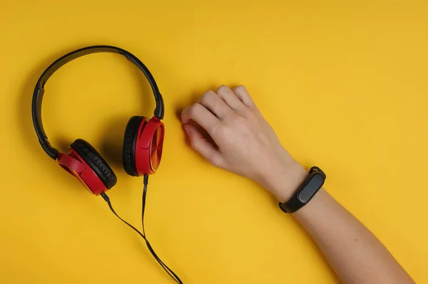 Wired headphones, female hand with smart bracelet on yellow background. Modern gadgets. Top view