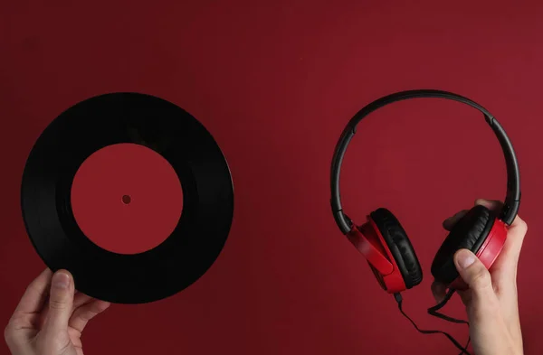 Female hands hold wired headphones with a vinyl record on red background. Retro style, DJ. Top view, minimalistic music concept.