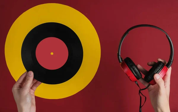 Female hands hold wired headphones with a vinyl record on red yellow background. Retro style, DJ. Top view, minimalistic music concept.