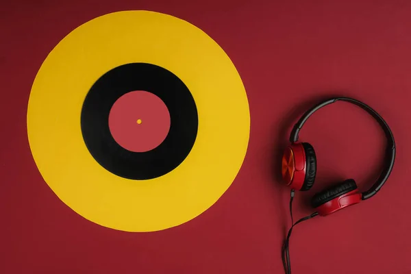 Wired headphones with a vinyl record on yellow red background. Retro style, DJ. Top view, minimalistic music concept.