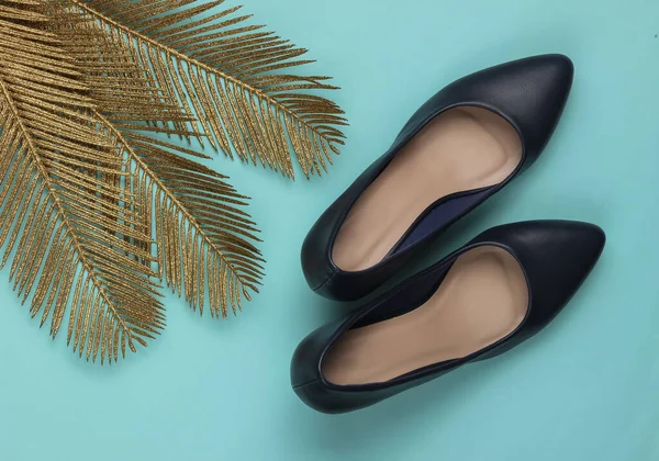 Minimalist moda hala hayattadır. Mavi pastel arka planda altın palmiye yaprakları olan klasik topuklu ayakkabılar. Stüdyo çekimi. Üst görünüm