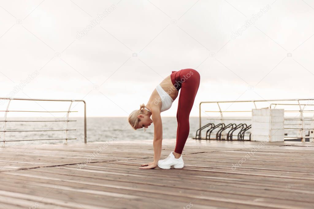 Morning workout. Healthy lifestyle concept. Young attractive woman in sportswear does warm up before exercise on the beach at sunrise. Stretching