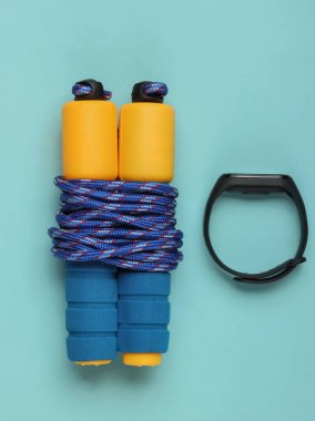 Mavi arka planda ip atlamak ve akıllı bilezik takmak. Spor aletleri. Üst Manzara. Fitness konsepti