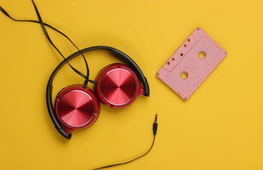 Sarı arka planda ses kaseti olan kablolu kulaklıklar. Retro tarzı DJ. Üst görünüm, minimalist müzik konsepti.