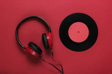 Kırmızı arka planda plak kaydı olan kablo kulaklıklar. Retro tarzı DJ. Üst görünüm, minimalist müzik konsepti.