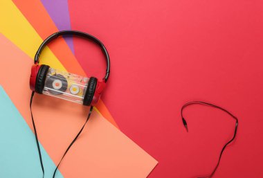 Renkli kağıt arka planda ses kaseti olan kablolu kulaklıklar. Retro tarzı DJ. Üst görünüm, minimalist müzik konsepti.