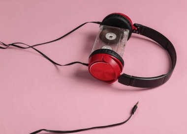 Pembe pastel arka planda ses kaseti olan kablolu kulaklıklar. Retro tarzı DJ. Minimalist müzik konsepti.