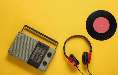 FM radyo alıcısı, eski tarz kulaklıklar, sarı arka planda vinil kayıt. Müzik aşığı konsepti. Üst Manzara. 70 'ler