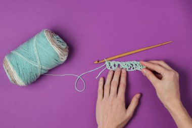 Kadın elleri ahşap örgü örer ve mor arka planda yün iplikler. Ev hanımı hobisi