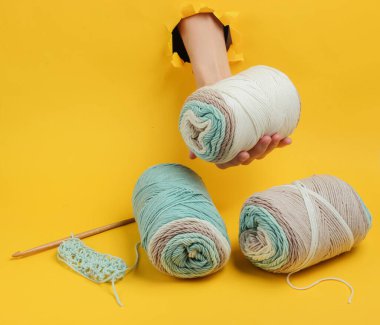 Sarı arka plandaki yırtık bir delikten yün iplik yumağını tutan kadınların eli. Ev Kadınları Hobileri. Yaratıcı minimalizm